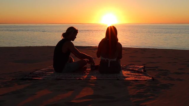 Young couple drinking beer on the beach during summer sunset