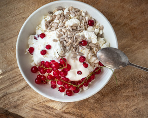 Light and tasty Breakfast with homemade cottage cheese, seeds and berry jam in a white deep plate with a spoon on a rough wooden background from close up