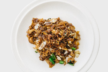 Overhead view of Malaysian wide rice noodle dish prepared in wok and served on white plate, isolated on white background