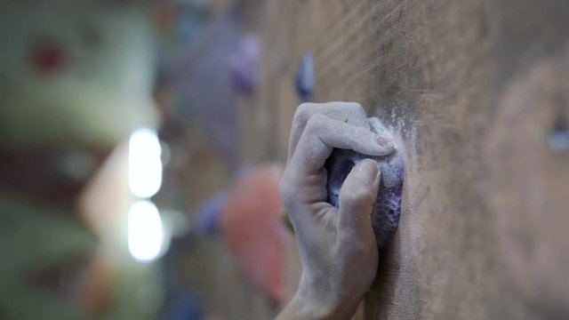 slow motion of rock climber hand in chalk, grabs the climbing stone while training in climbing gym. chalky climbers fingers on the holds