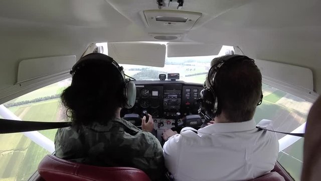 Two pilots flying in a Cessna airplane. One dressed in the regular aviation clothes, the other is dressed in a camouflaged army outfit.
