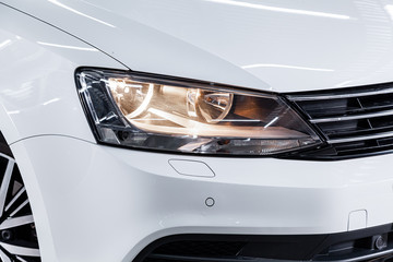 Close-up of the white headlight, bumper, wheel. Halogen headlight on a new car