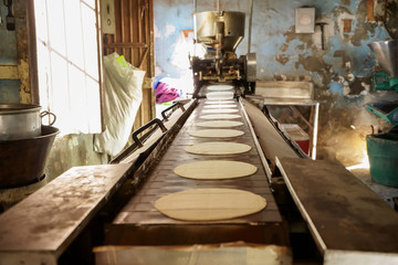 Están saliendo las tortillas de maíz de la maquina antigua en un pueblo de México.