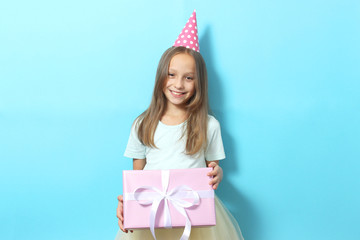 Portrait of a little girl in a festive cap and with a gift in her hands on a colored background. Birthday, presents, holiday