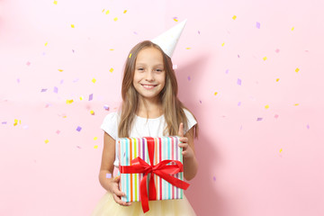 Portrait of a little girl in a festive cap and with a gift in her hands on a colored background....