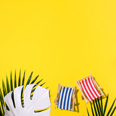 Deck chairs with hard shadow, monstera and palm leaves on yellow paper background. Flat lay and copy space. Summer travel vacation concept. Minimal composition