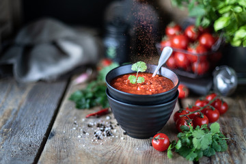 Group of red cherry tomatoes as an ingredient for tomato sauce in a black bowl on a wooden table.
