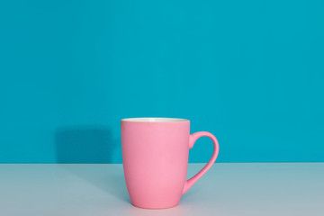 Pink cup on light surface on bright blue background