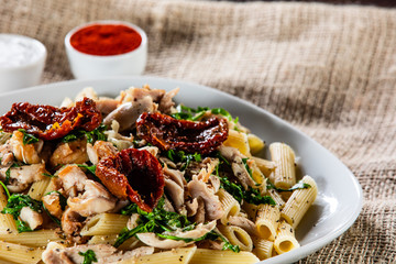 Pasta with chicken meat, sun-dried tomatoes and rucola