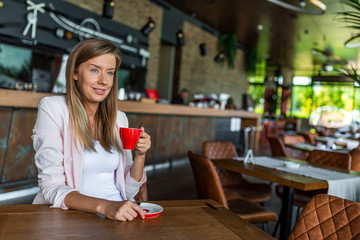 Portrait of woman smiling in coffee shop cafe vintage color tone. Smiling woman in a good mood with cup of coffee sitting in cafe. Bright sunny morning. Young woman sips coffee in coffee shop