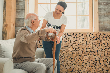 Fototapeta premium Woman volunteer supporting old man rising from sofa