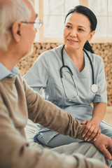 Calm woman in blue nurse uniform touching hand of ward