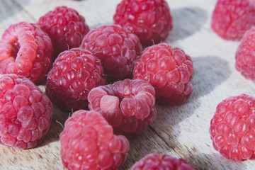 Fresh organic raspberries background closeup. Fresh raspberries on wooden background; berries are lit with the daylight