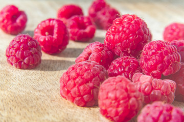 Fresh organic raspberries background closeup. Fresh raspberries on wooden background; berries are lit with the daylight