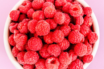 Fresh organic raspberries in a white metal bucket on pink background