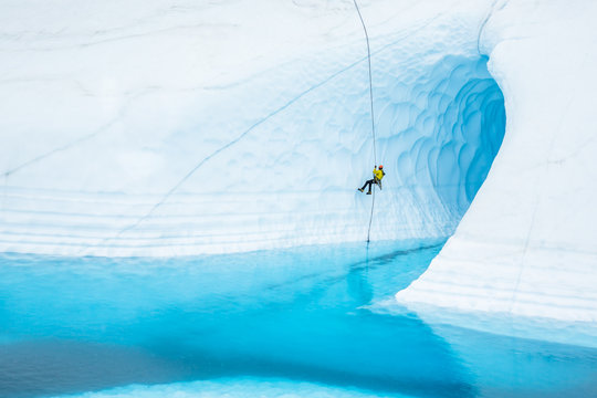 Rappeling in front of a large ice cave flooded with a blue pool on the Matanuska Glacier in Alaska