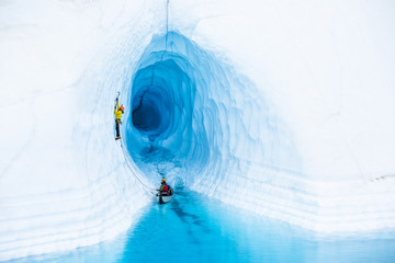 Ice cimber in front of an ice cave leading up from a canoe in a blue pool on the Matanuska Glacier.