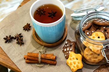 Winter theme. Christmas tea with spices, cup of tea with cinnamon, anise, cookies in a shape of star on wooden background linen napkin. Mug of tea with Christmas decoration