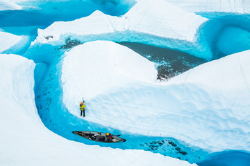 Ice climber and a canoe near an island of ice in a blue pool on the Matanuska Glacier in Alaska.