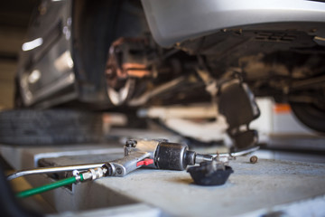 Car repair in the service station. Hands of a mechanic in overalls repairing the car on the lift without wheel, holding the tire and mechanical works.