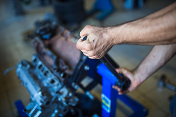 Mechanic with a tool in his hands repairing the motor of the machine. The process of working in the service station