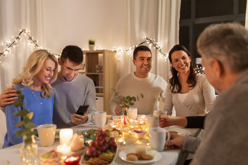 family, holidays and people concept - happy couple with smartphone having tea party at home