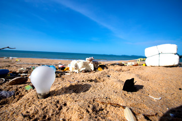 Fototapeta na wymiar Light blub, glass bottles and garbage waste on the beach
