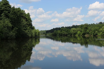 Clouds are reflected in the river. Sunny windless weather. Peace and silence. Natural beauty.
