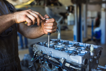 Mechanic with a tool in his hands repairing the motor of the machine. The process of working in the service station