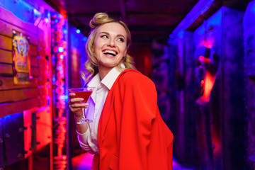 Photo of happy blonde with cocktail in her hand on red and blue background