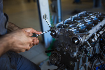 Mechanic with a tool in his hands repairing the motor of the machine. The process of working in the service station