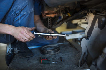 Car repair in the service station. Hands of a mechanic in overalls repairing the car on the lift without wheel, holding the tire and mechanical works.