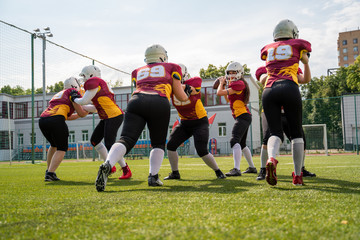 Full-length image of sportive women playing american football on green lawn