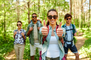 travel, tourism, hike and people concept - group of friends with backpacks and woman showing thumbs up gesture in forest