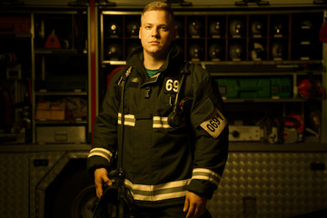 Full-length image of young firefighter man with helmet in his hand looking into camera while
