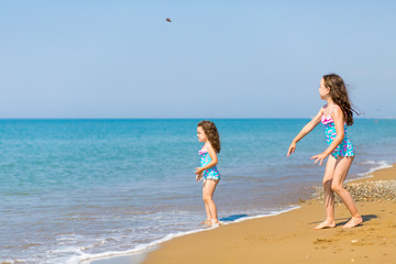 little girls in bright swimsuits play on the beach. Children on vacation. Family vacation. happy sisters