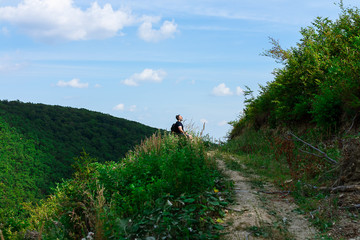 Top of the hill, trail leading to the top and one lonely male figure sitting and relaxing after the hike