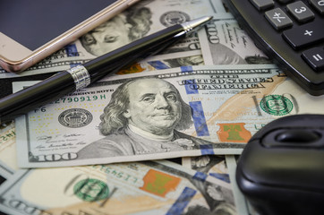 Fototapeta premium smartphone and pen, part of a calculator and a computer mouse on dollars. Close-up.