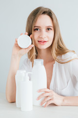 Young beautiful girl with white cosmetic bottles of different sizes