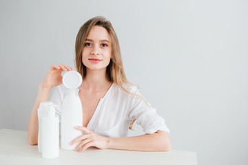 Young beautiful girl with white cosmetic bottles of different sizes