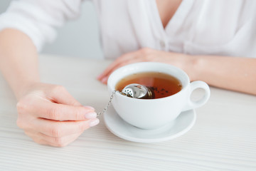 Young beautiful girl brews tea in a useful reusable metal strainer