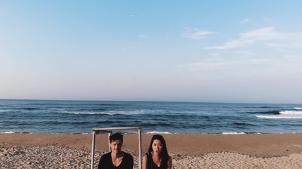 Drone Aerial footage of young biracial couple sitting together on a beach at sunset - romantic