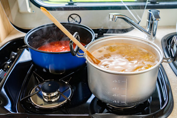 Motorhome cooking - Tomato sauce with spinach in a blue saucepan together with dried pasta in a grey saucepan boiling away on the hob