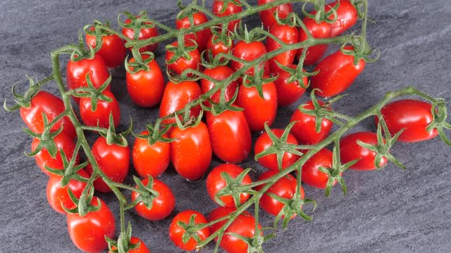  Ripe red datterino tomatoes rotating on grey stone. Top view, shot in 4K.