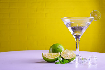 Vermouth in a martini glass and a slice of lime on a yellow background, copy space.