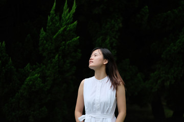 One Asian girl in pure white skirt, standing in front of pine tree under natural sunlight....