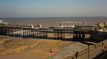 Fototapeta premium A high up view of the sea front promenade and first part of Cromer pier, Norfolk. UK weather: A bright and sunny, but breezy day, with bright blue skies and light stratus clouds.