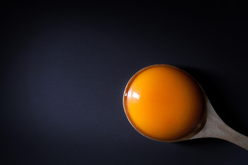Egg yolk on a wooden spoon on black background with space for copy