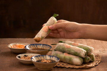 Young woman's hands eating healthy spring roll dipped in a soya sauce. Selective focus.