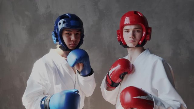 Multi ethnic. Two brave and confident boxers in a kimono, in fighting gloves and protective helmets of red and blue. They are decisive and unshakable. Looking at the camera